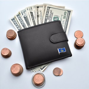 May include: A black leather wallet with a small flag pin on the front. The wallet is open and filled with US dollar bills. There are stacks of copper coins scattered around the wallet.