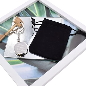 May include: A silver key chain with a round charm that says "Merry Christmas & a Happy New Year Charlotte". The keychain is in a white frame with a green and white background. The keychain is also in a small black velvet bag.