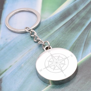 May include: Silver compass keychain with a compass rose design and the letters N, S, E, and W engraved on the face.