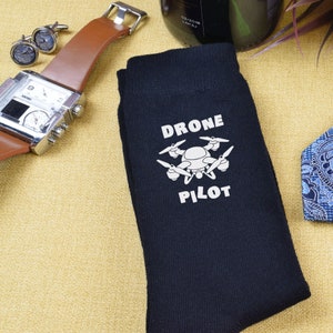 May include: A pair of black socks with a white drone graphic and the text "Drone Pilot".