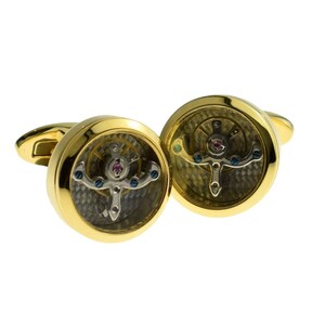 May include: Gold cufflinks with a clear, round face that reveals a working watch mechanism with blue and pink accents.