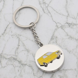 Puede incluir: Un llavero plateado con un dije redondo que presenta una camioneta amarilla con techo blanco y ruedas negras.