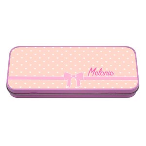 Puede incluir: Un estuche de lápices de metal rosa con un patrón de corazones blancos y un lazo rosa. El nombre "Melanie" está impreso en el estuche.