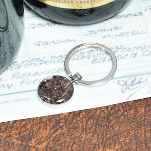 May include: A silver key ring with a round, clear, resin charm containing brown and white flecks. The charm is attached to a silver key ring.
