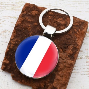 Puede incluir: Un llavero plateado con un encanto redondo azul, blanco y rojo de la bandera francesa.