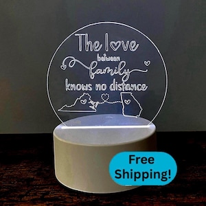 May include: A clear acrylic LED night light with the text "The love between family knows no distance." The design includes outlines of the states of Virginia and Georgia, connected by a dotted line and hearts. The base is a light gray color.