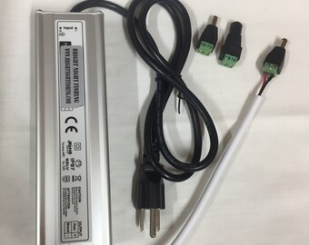 Puede incluir: Una fuente de alimentación plateada con un cable de alimentación negro y tres enchufes de conexión verde y negro. La fuente de alimentación tiene el texto "BRIGHT NIGHT FISHING" y "WWW.BRIGHTNIGHTFISHING.COM" impreso en ella. La fuente de alimentación también tiene el texto "CE", "ROHS IP67", "SELV", "CAUTION", "ATTENTION" y "OUTPUT" impreso en ella.