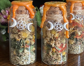 May include: Three glass jars filled with dried herbs and flowers. Each jar has a cork stopper sealed with orange wax. Silver charms with crescent moons and a pentacle are attached to the jars. The text "@paintedwitchdesigns" is at the bottom.