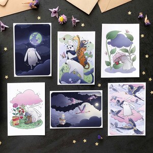 May include: Set of six illustrated cards featuring a white rabbit in different scenes. The cards are printed on white cardstock and have a matte finish. The scenes include a rabbit flying in the night sky, a rabbit under a cloud, a rabbit in a forest, a rabbit in a field, a rabbit in a garden, and a rabbit in a sky with birds.
