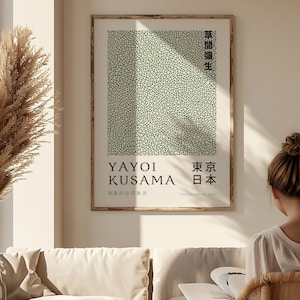Puede incluir: Un póster minimalista con un patrón de lunares verdes y el texto "Yayoi Kusama" y "Tokio, Japón, 1967". El póster está enmarcado en madera y colgado en una pared blanca.