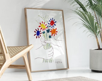 May include: A framed print of a colorful bouquet of flowers with two hands holding the stems. The print is on a white background and has the artist's signature and date in the bottom right corner.