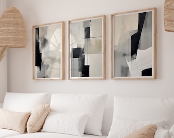 May include: Three abstract art prints in black, white, and beige frames hang on a white wall above a white sectional sofa with beige throw pillows and a black throw blanket.
