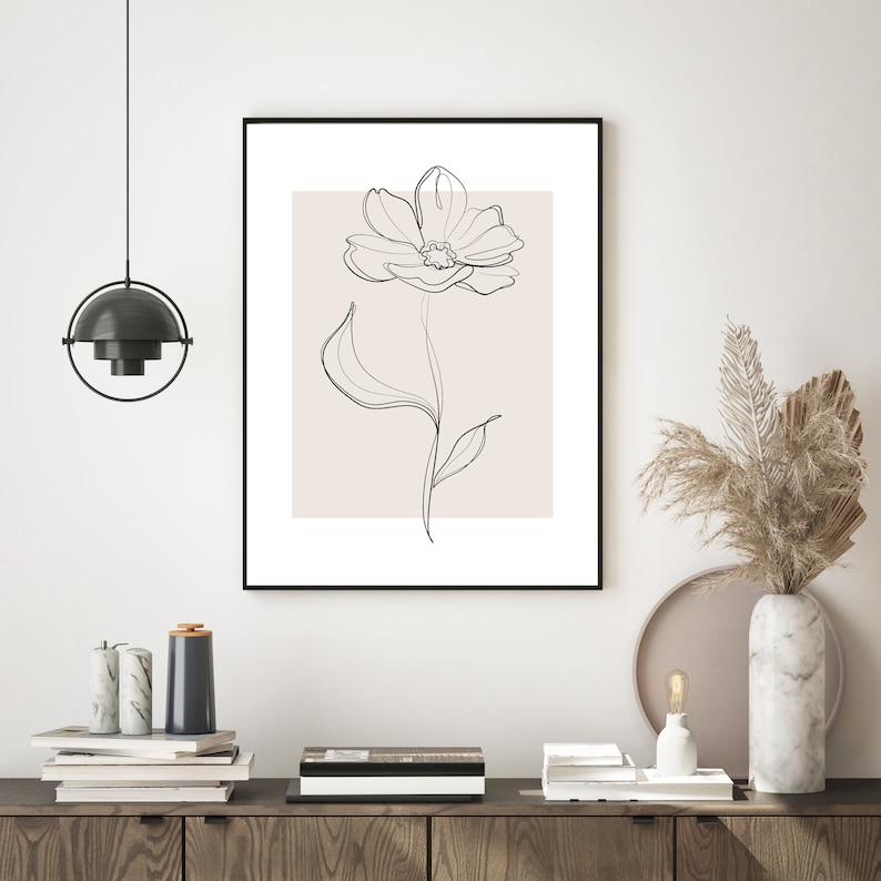 May include: A black framed print of a line drawing of a flower with a beige background.