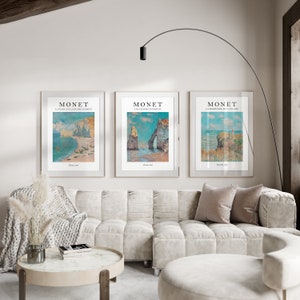 Puede incluir: Tres impresiones de arte enmarcadas de paisajes marinos de Claude Monet. Las impresiones est&aacute;n en marcos blancos y presentan el texto "MONET" y el t&iacute;tulo de cada pintura. Las pinturas son "La Plage et la falaise d'Etretat", "Les falaises d'Etretat" y "A la Promenade sur la falaise".