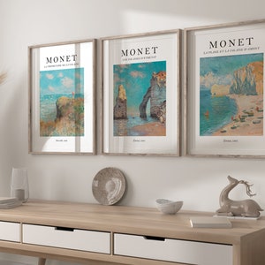 Puede incluir: Tres impresiones de arte enmarcadas de paisajes marinos de Claude Monet. Las impresiones est&aacute;n en marcos de madera con un passe-partout blanco. Las impresiones presentan el texto "MONET" y el t&iacute;tulo de cada pintura.