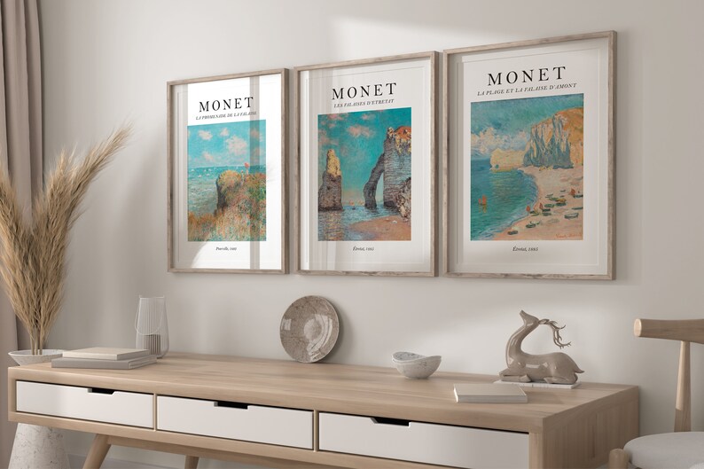 Puede incluir: Tres impresiones de arte enmarcadas de paisajes marinos de Claude Monet. Las impresiones est&aacute;n en marcos de madera con un passe-partout blanco. Las impresiones presentan el texto "MONET" y el t&iacute;tulo de cada pintura.