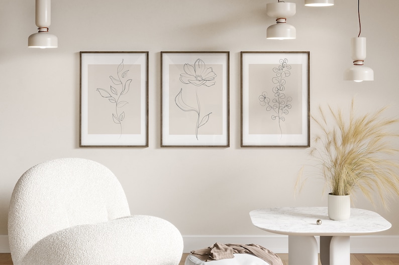 May include: Three framed minimalist line drawings of flowers and plants on a beige wall. The drawings are in black and white and are set against a light beige background. The frames are brown wood.