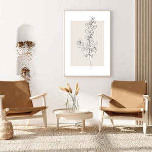 May include: Two brown leather chairs with wooden frames, a small round wooden table with a glass top, and a framed print of a black line drawing of a plant on a beige background. The chairs and table are on a light beige rug in a room with white walls.