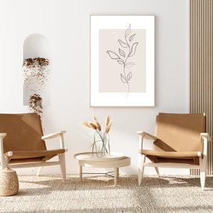 May include: Two brown leather chairs with wooden frames and a wooden coffee table with a vase of dried grass in the center. A framed print of a line drawing of a plant hangs on the wall behind the table.