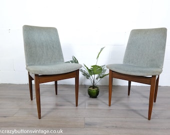 May include: Two mid-century modern chairs with light blue upholstered seats and wooden frames. The chairs have a simple, elegant design with tapered legs. A small potted plant sits between the chairs.