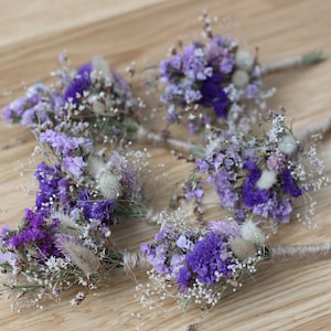 Puede incluir: Seis pequeños ramos de flores secas en tonos de morado y blanco, atados con cuerda. Los ramos están dispuestos sobre una superficie de madera.