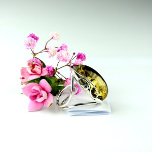 May include: A silver ring with a large, teardrop-shaped amber stone. The ring is surrounded by pink flowers.