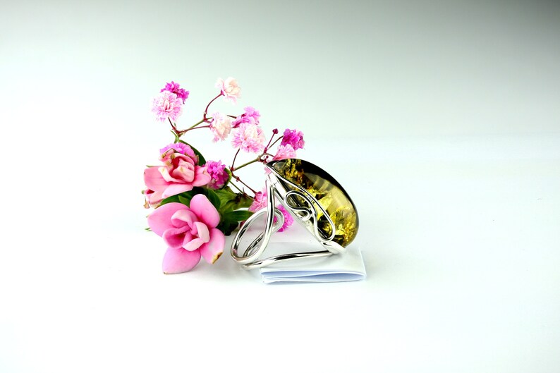 May include: A silver ring with a large, teardrop-shaped amber stone. The ring is surrounded by pink flowers.