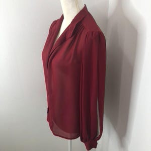 K&ouml;nnte beinhalten: Eine lang&auml;rmelige, burgunderfarbene Bluse mit Kragen und Knopfleiste. Die Bluse ist aus einem durchsichtigen Stoff gefertigt und hat eine leicht lockere Passform.