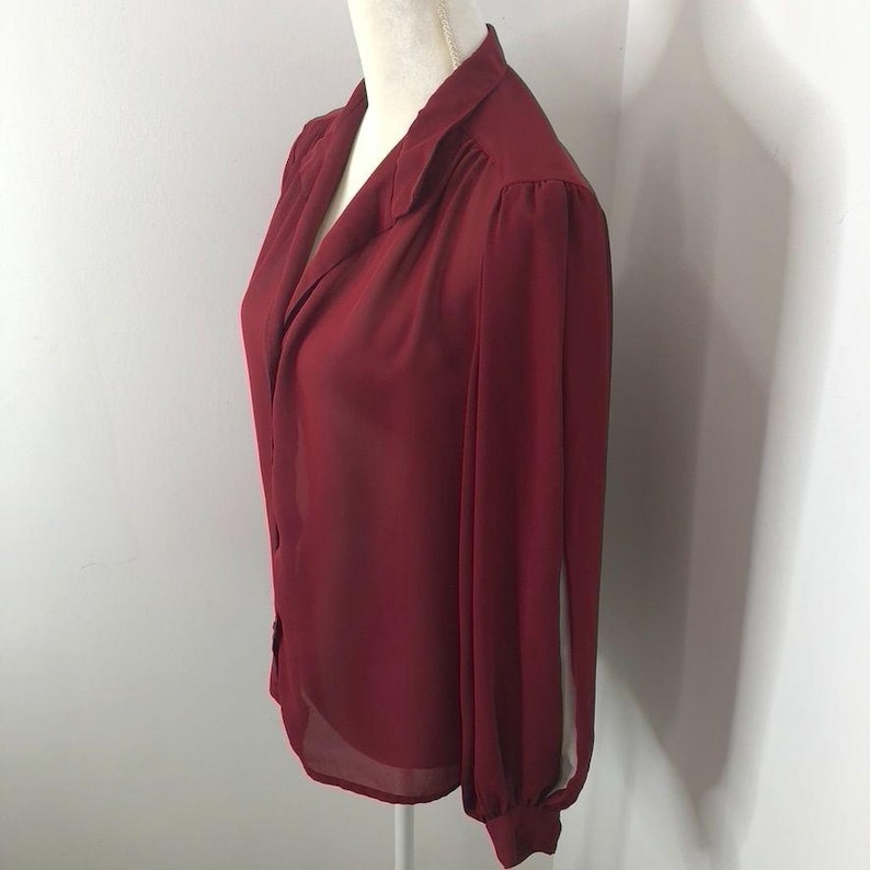 K&ouml;nnte beinhalten: Eine lang&auml;rmelige, burgunderfarbene Bluse mit Kragen und Knopfleiste. Die Bluse ist aus einem durchsichtigen Stoff gefertigt und hat eine leicht lockere Passform.