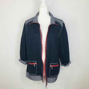 May include: A navy blue zip-up jacket with white and blue striped trim and red zipper. The jacket has two pockets with red zipper pulls.