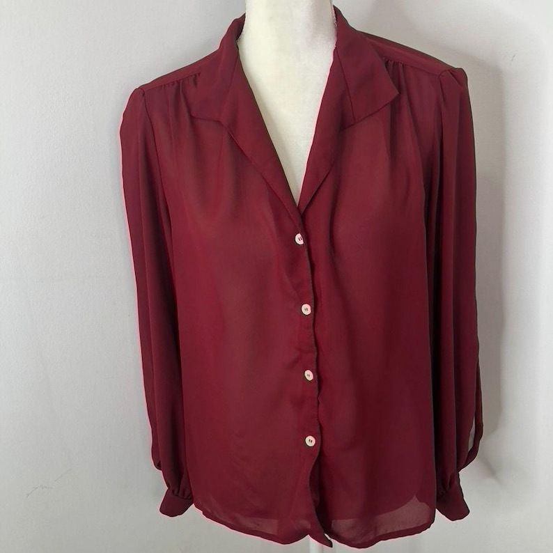 K&ouml;nnte beinhalten: Eine lang&auml;rmelige Bluse in Burgunderrot mit Knopfleiste und Kragen. Die Bluse ist aus einem durchsichtigen Stoff.