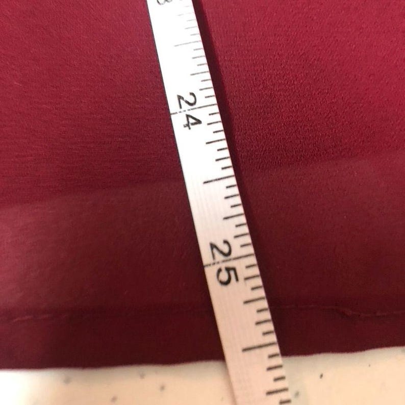 K&ouml;nnte beinhalten: Nahaufnahme eines roten Stoffes mit einem wei&szlig;en Ma&szlig;band, das 24 und 25 Zoll anzeigt.