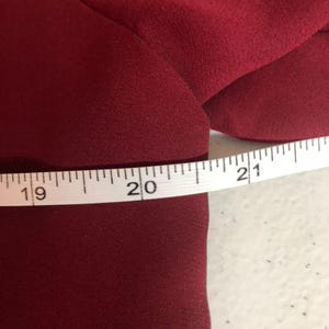 K&ouml;nnte beinhalten: Nahaufnahme eines burgunderfarbenen Stoffes mit einem wei&szlig;en Ma&szlig;band, das 19, 20 und 21 Zoll anzeigt.
