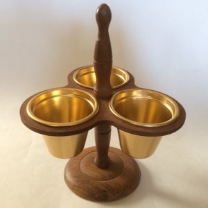 May include: A wooden condiment holder with three gold-colored bowls. The holder has a round base and a tall handle.
