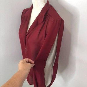 K&ouml;nnte beinhalten: Eine &auml;rmellose Bluse in Burgunderrot mit Kragen und Knopfleiste. Die Bluse hat einen Schlitz an den Seiten der &Auml;rmel.