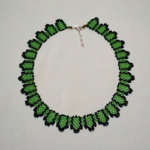 May include: A beaded necklace with a repeating leaf design. The leaves are bright green with black beaded borders. The necklace has a silver clasp and is shown against a pale background.