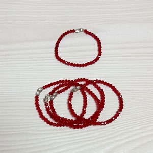 May include: Two red crystal bead bracelets with silver clasps. The smaller bracelet is on top of the larger bracelet.