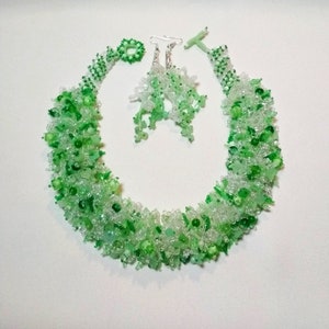 May include: A beaded jewelry set featuring a necklace, earrings, and a ring. The set is composed of clear and green beads, creating a textured, organic appearance. The necklace has a toggle clasp. The earrings have silver hooks.