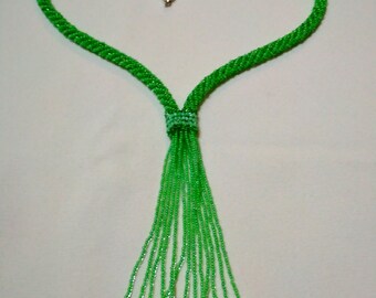 May include: A green beaded necklace in the shape of a heart. The necklace features a tassel of beaded strands and a silver clasp. The beads are a vibrant shade of green.