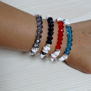 Pode incluir: Quatro pulseiras de contas em tons de cinza, azul marinho, vermelho e turquesa. Cada pulseira apresenta contas facetadas e detalhes brancos de formato irregular. As pulseiras são exibidas em uma superfície clara.