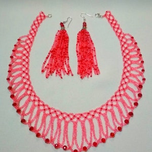 May include: A pink beaded necklace and matching earrings set. The necklace features a delicate, openwork design with red accents. The earrings have long, red beaded tassels, creating a coordinated jewelry set.