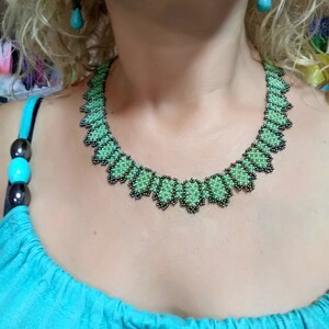 May include: A green and black beaded necklace and matching earrings. The necklace has a scalloped edge. The earrings feature turquoise-coloured teardrop-shaped beads.