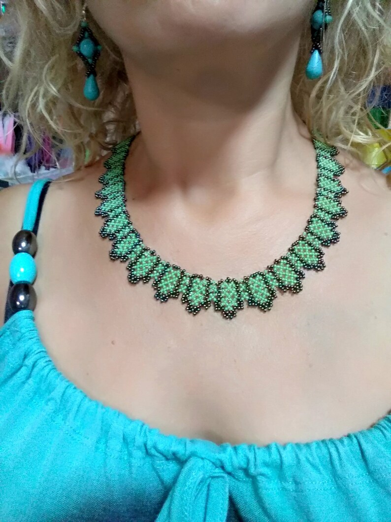 May include: A green and black beaded necklace and matching earrings. The necklace has a scalloped edge. The earrings feature turquoise-coloured teardrop-shaped beads.