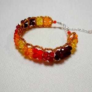 Könnte beinhalten: Ein farbenfrohes Perlenarmband mit einem Farbverlauf von Dunkelrot bis Gelb. Das Armband besteht aus kleinen, facettierten Perlen, die mit goldfarbenem Draht aufgefädelt sind. Der Verschluss ist silberfarben.