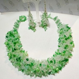May include: A beaded necklace and matching earrings set. The jewelry features a mix of clear and various shades of green beads. The necklace is a collar style, and the earrings dangle. The jewelry is displayed on a white surface.