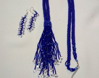May include: A blue beaded necklace and matching earrings set. The necklace features a long, braided design with a tassel of dangling beads and clear crystal accents. The earrings are a similar design, with clear crystal beads.