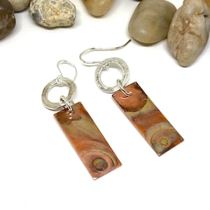 May include: A pair of silver and copper earrings with a marbled copper rectangle pendant and a silver circle.