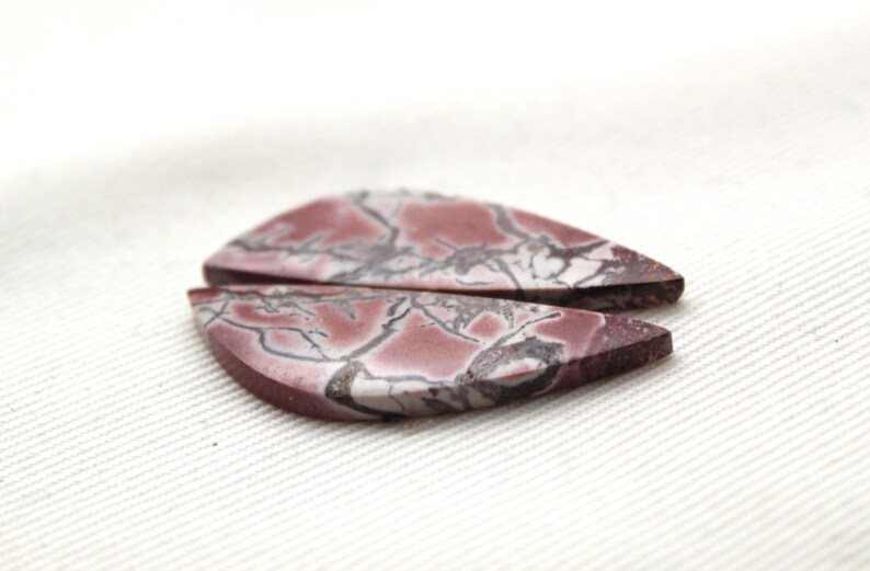 May include: Two teardrop-shaped cabochons featuring a deep mauve and reddish-brown base color with intricate, dark gray to black veining patterns running throughout the surface of the stones, displaying a smooth, polished, and flat top finish.