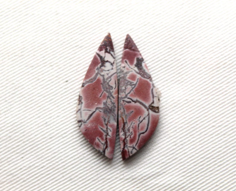 May include: Two matching marquise-shaped cabochons featuring a dusty rose and mauve base color with intricate, dark brown to black web-like veining patterns throughout the surface of each stone, creating a symmetrical pair of polished gemstones.