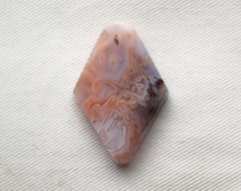May include: A diamond-shaped agate cabochon with a white, brown, and orange pattern. The stone has a translucent appearance and shows intricate details.
